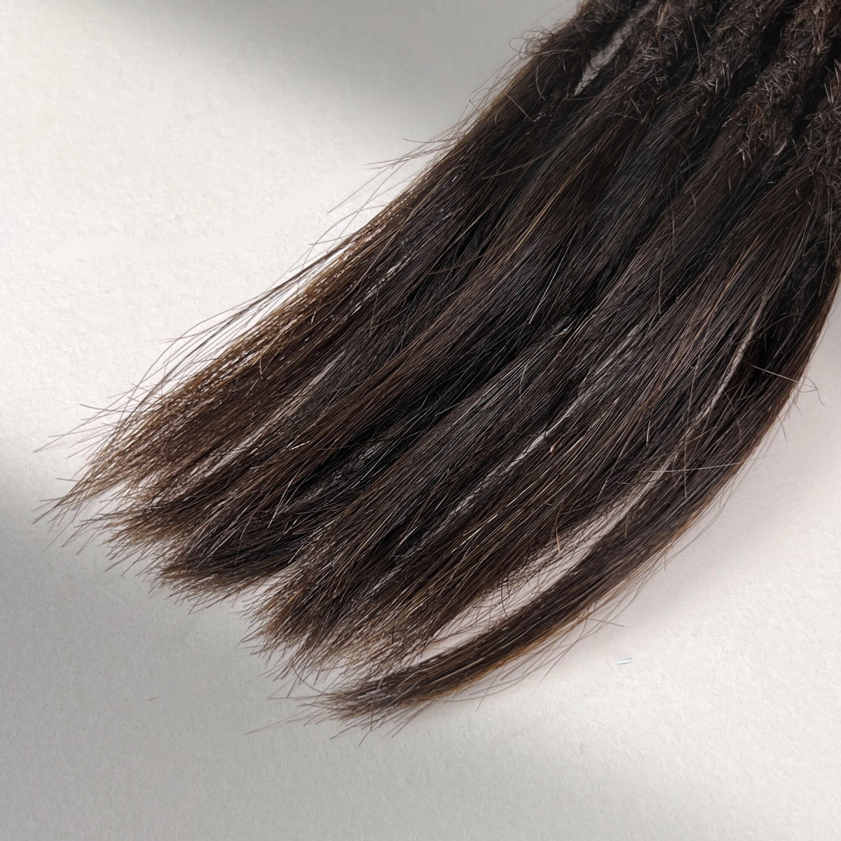 Tip detail of straight loc extensions with open ends in Warm Caramel Brown.