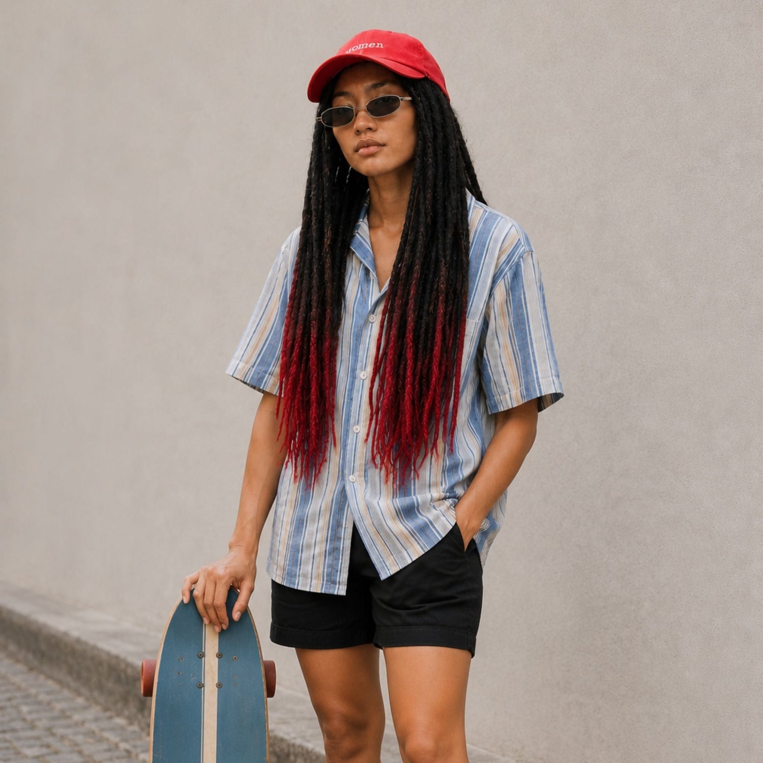 Community model wearing black straight loc extensions with a red ombré effect, styled with a striped shirt, shorts and a skateboard.