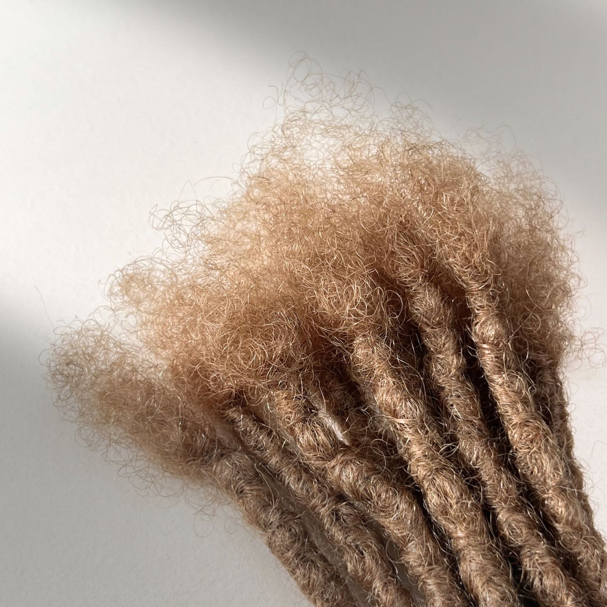 Connection point of kinky loc extensions with blunt ends in Dark Blonde, made using the interlocking method.
