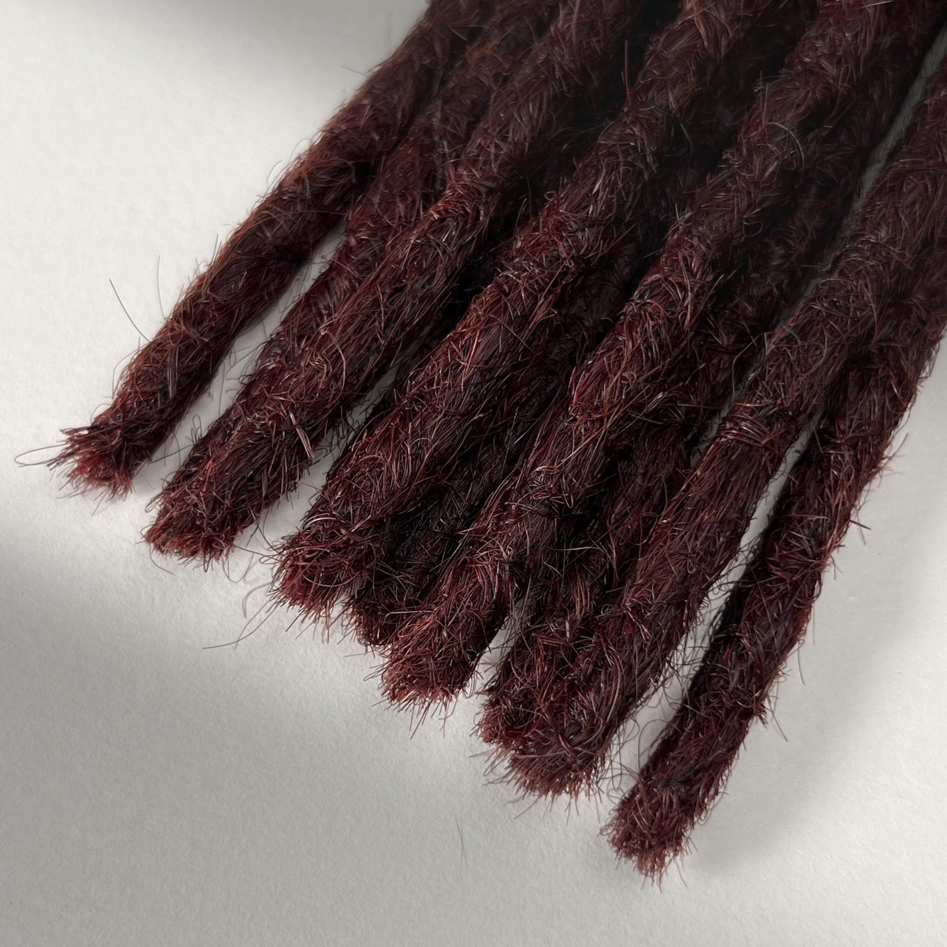 Tip detail of straight loc extensions with blunt ends in Rich Burgundy Red.