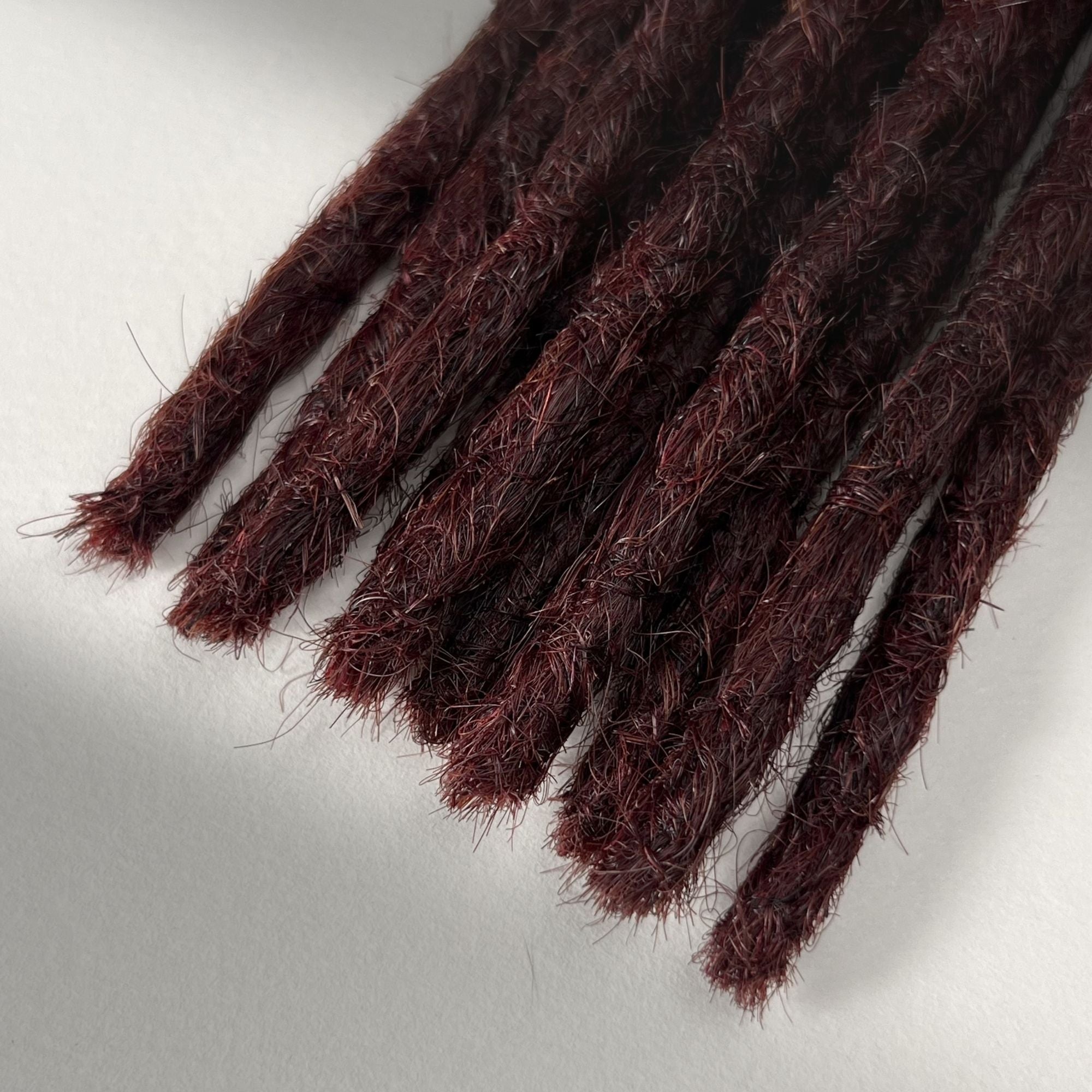 Tip detail of straight loc extensions with blunt ends in Rich Burgundy Red.