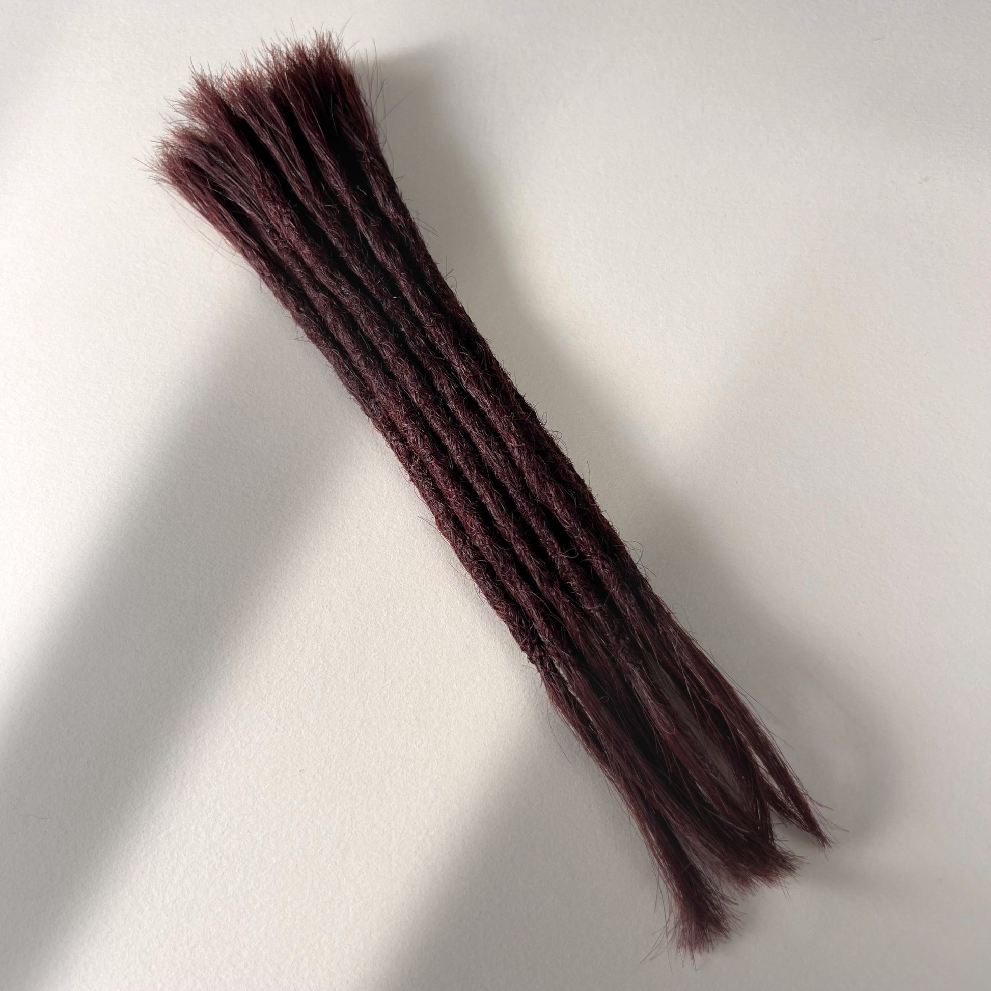 Full view of permanent straight loc extensions with open ends in Deep Crimson Red.