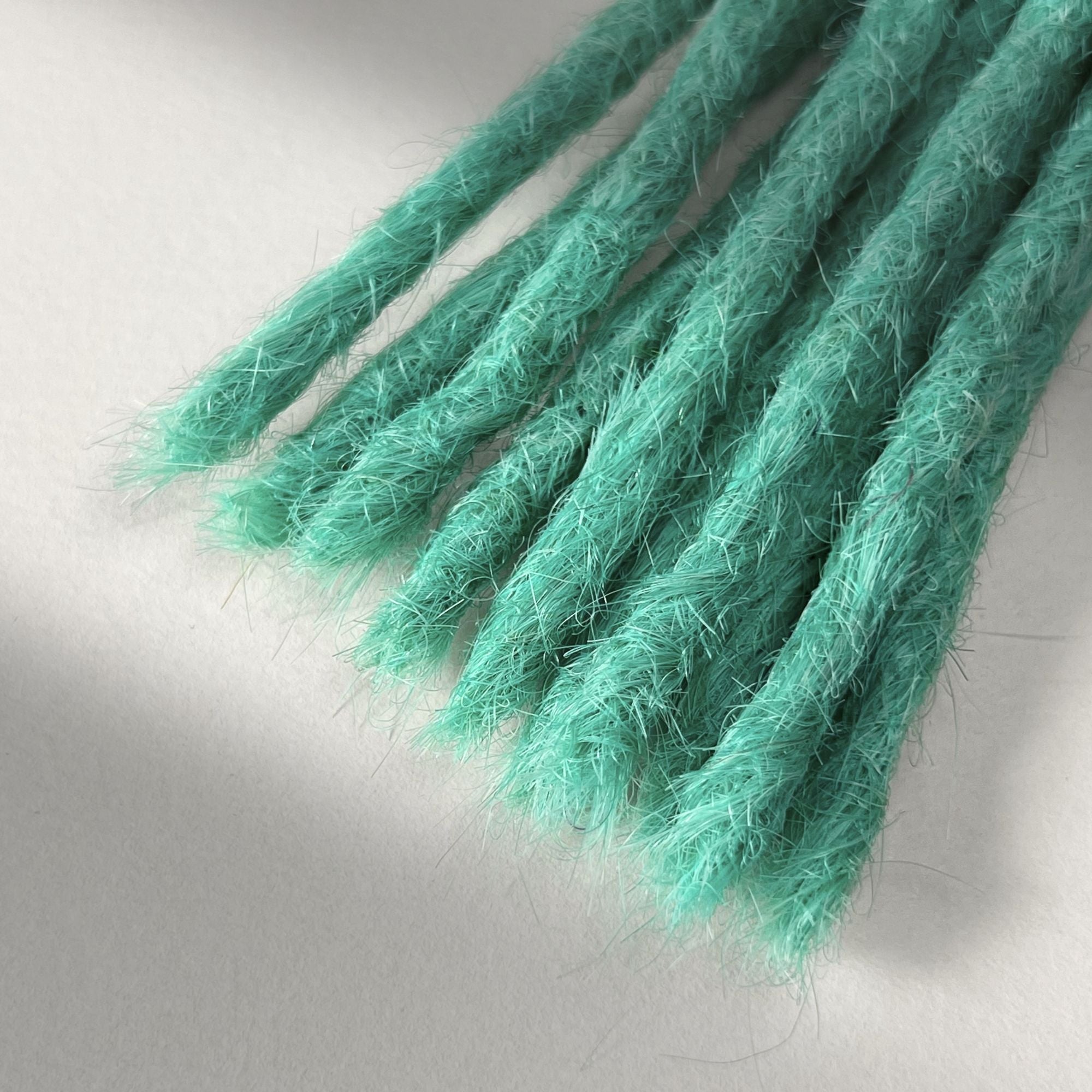 Tip detail of straight loc extensions with blunt ends in Pastel Emerald Green.