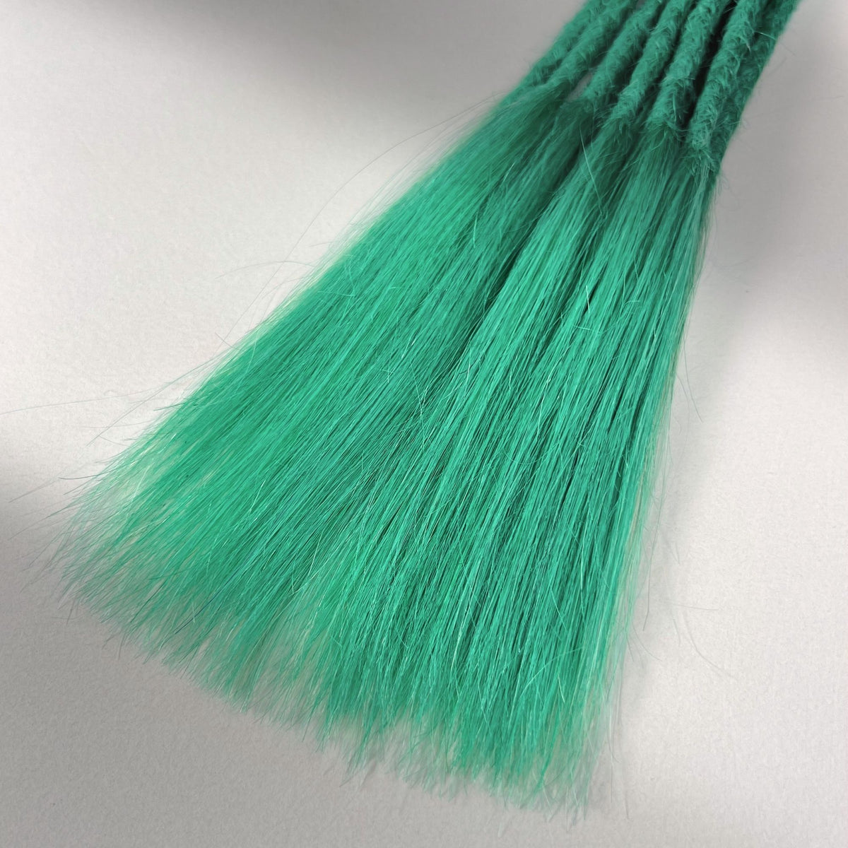 Tip detail of straight loc extensions with long loose ends in Pastel Emerald Green.