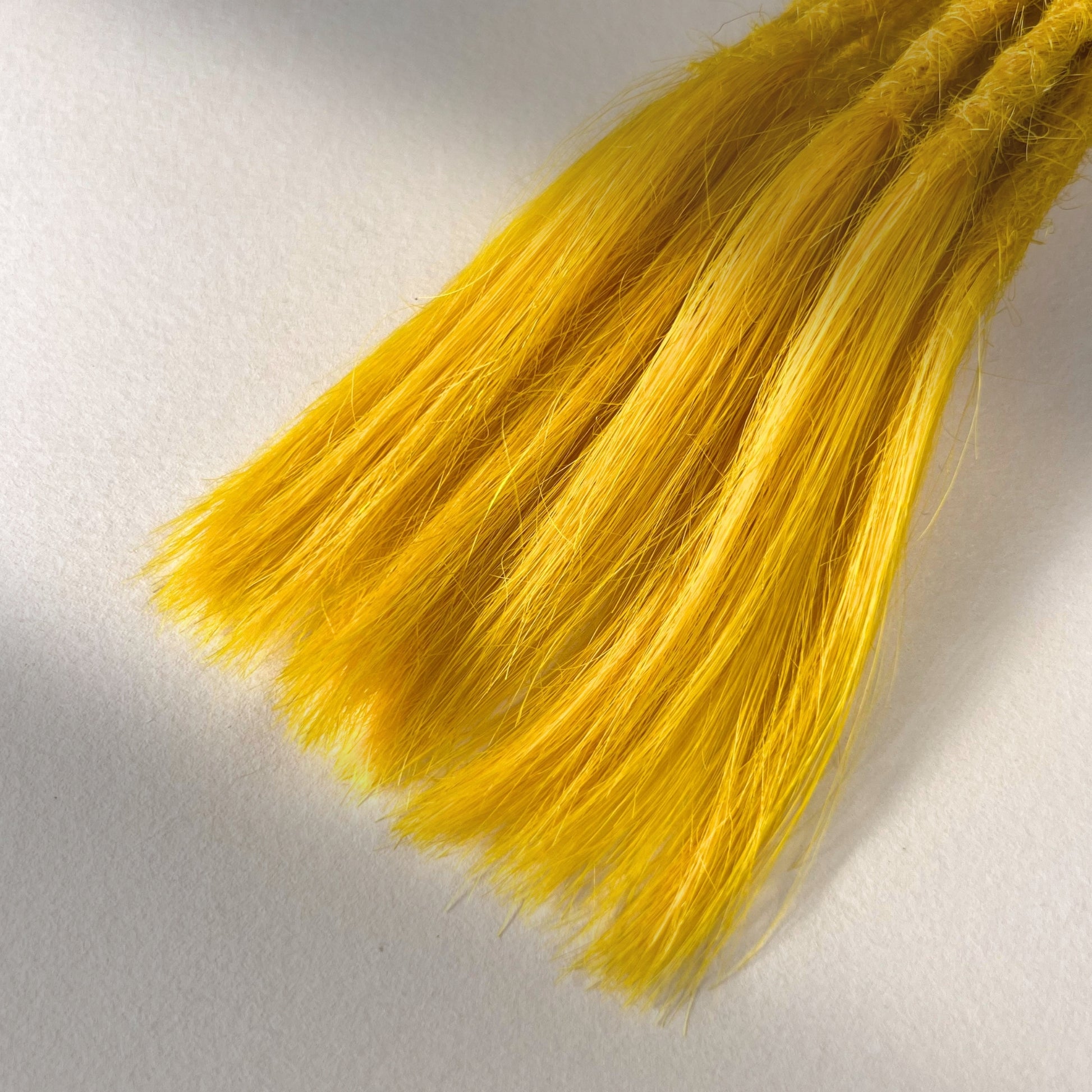 Tip detail of straight loc extensions with open ends in Lemon Yellow.