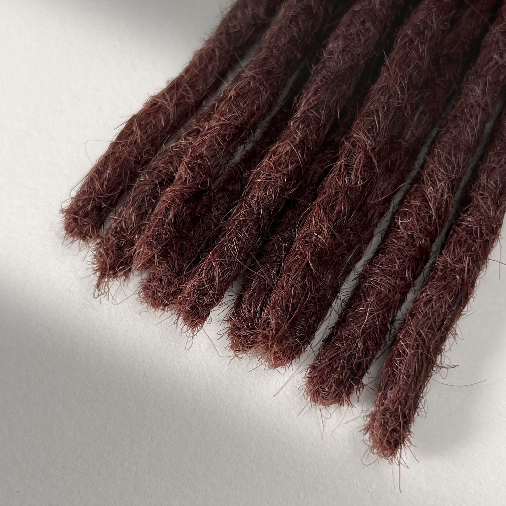 Tip detail of straight loc extensions with blunt ends in Warm Mahogany Red.