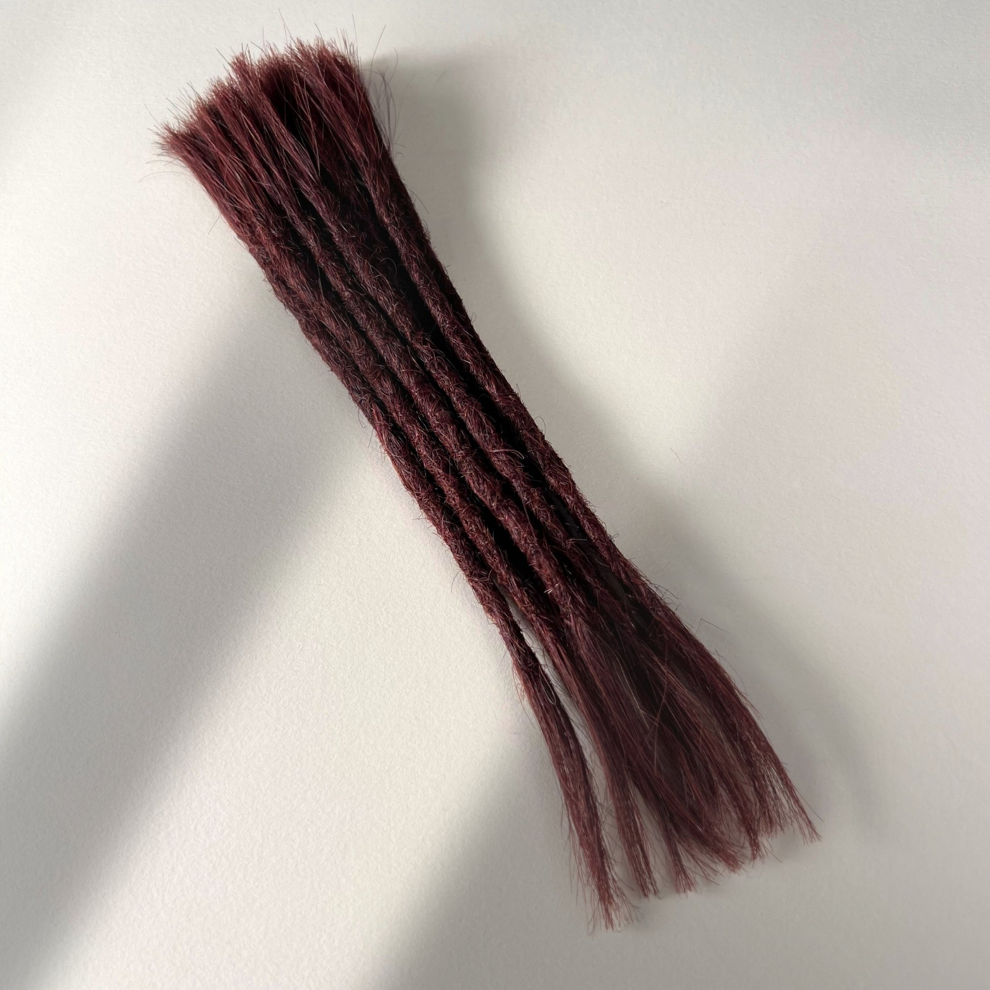 Full view of permanent straight loc extensions with open ends in Warm Mahogany Red.