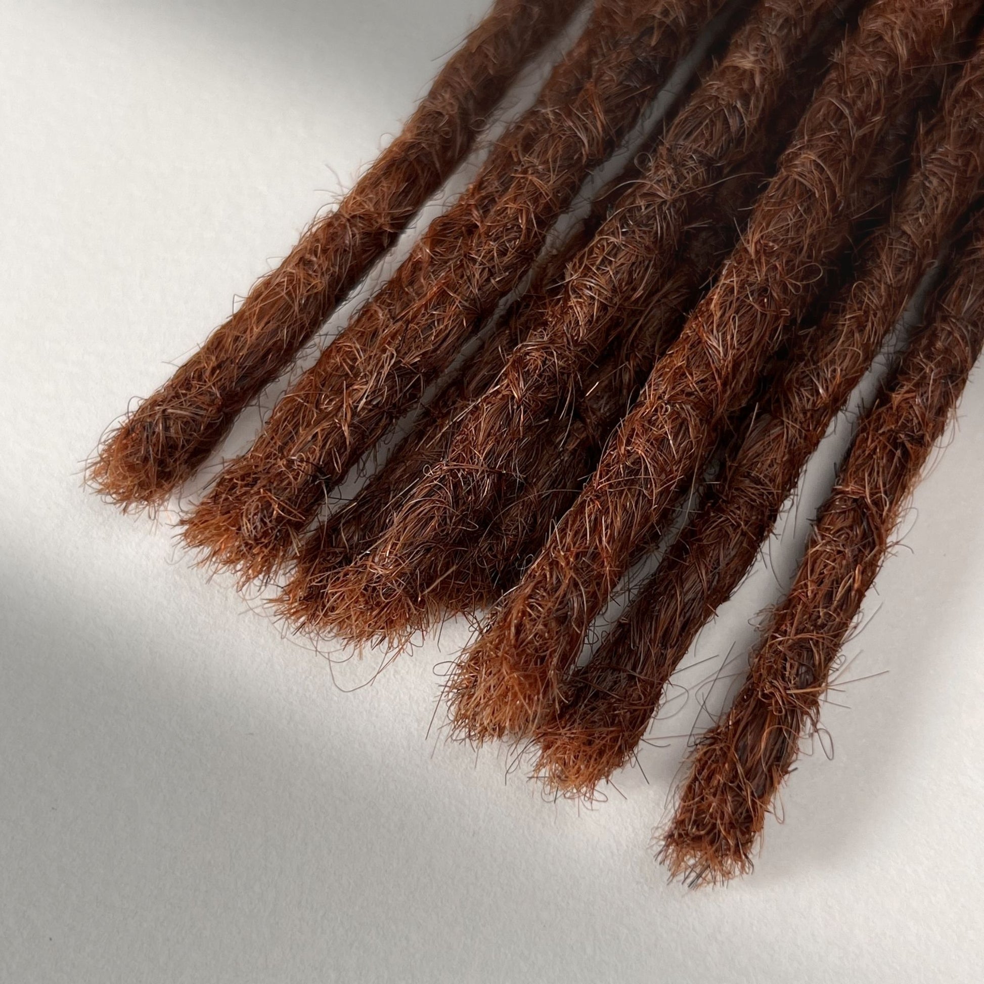 Tip detail of straight loc extensions with blunt ends in Warm Maple Copper.