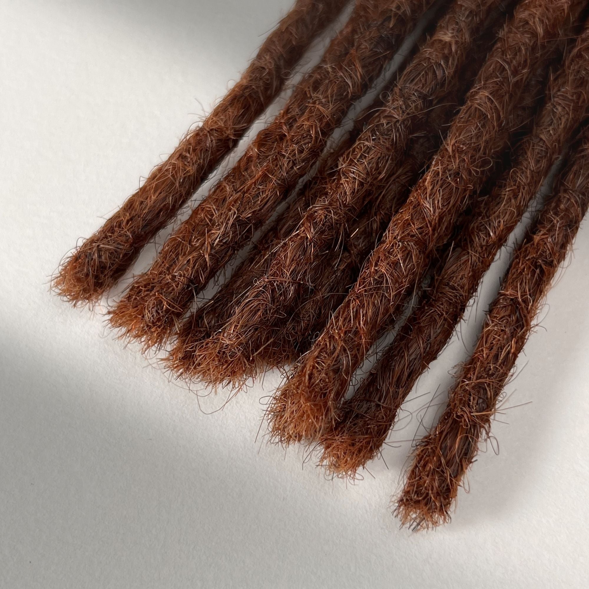 Tip detail of straight loc extensions with blunt ends in Warm Maple Copper.