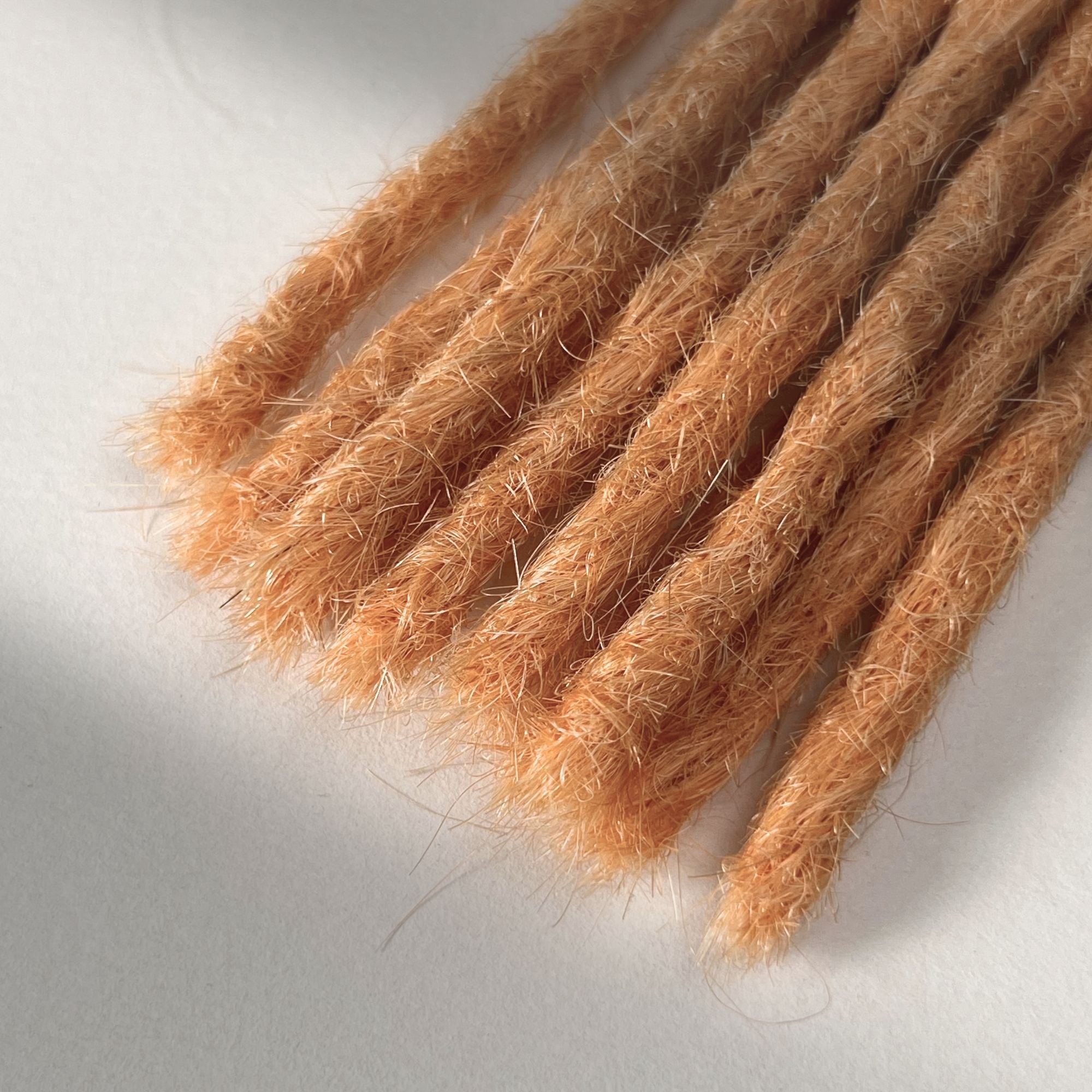 Tip detail of straight loc extensions with blunt ends in Peach Orange.