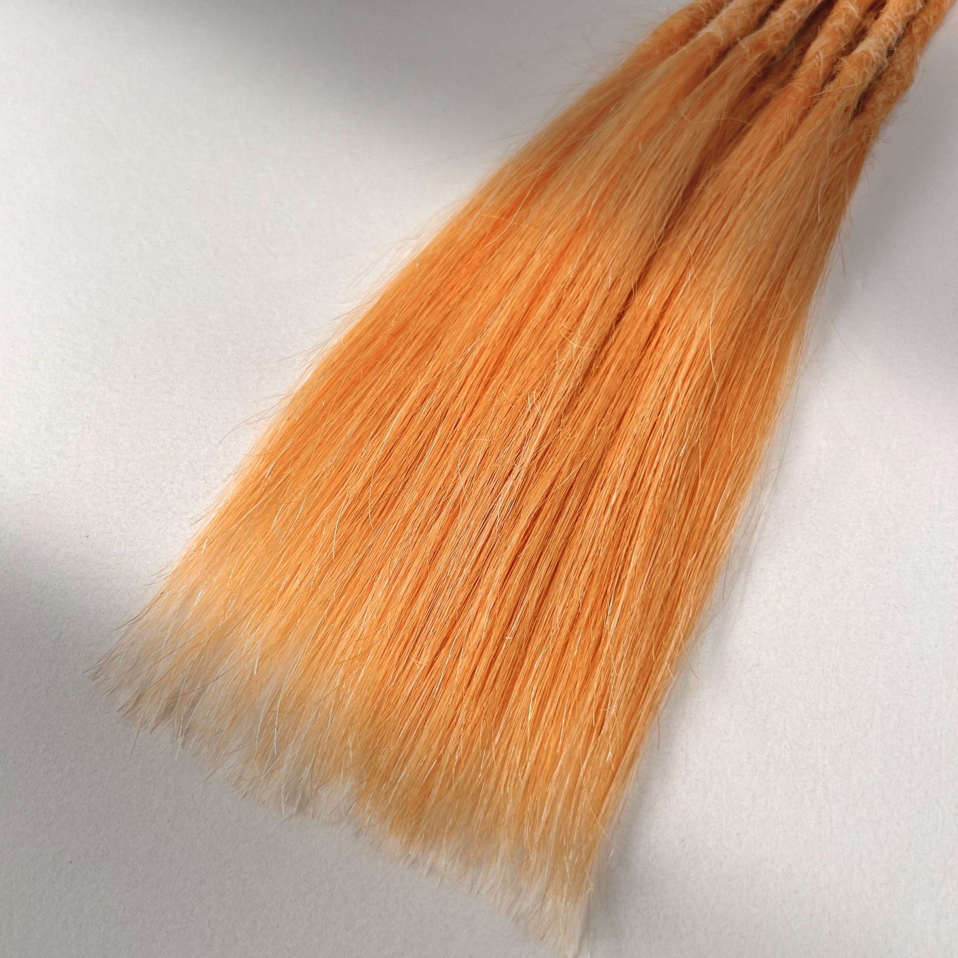 Tip detail of straight loc extensions with long loose ends in Peach Orange.