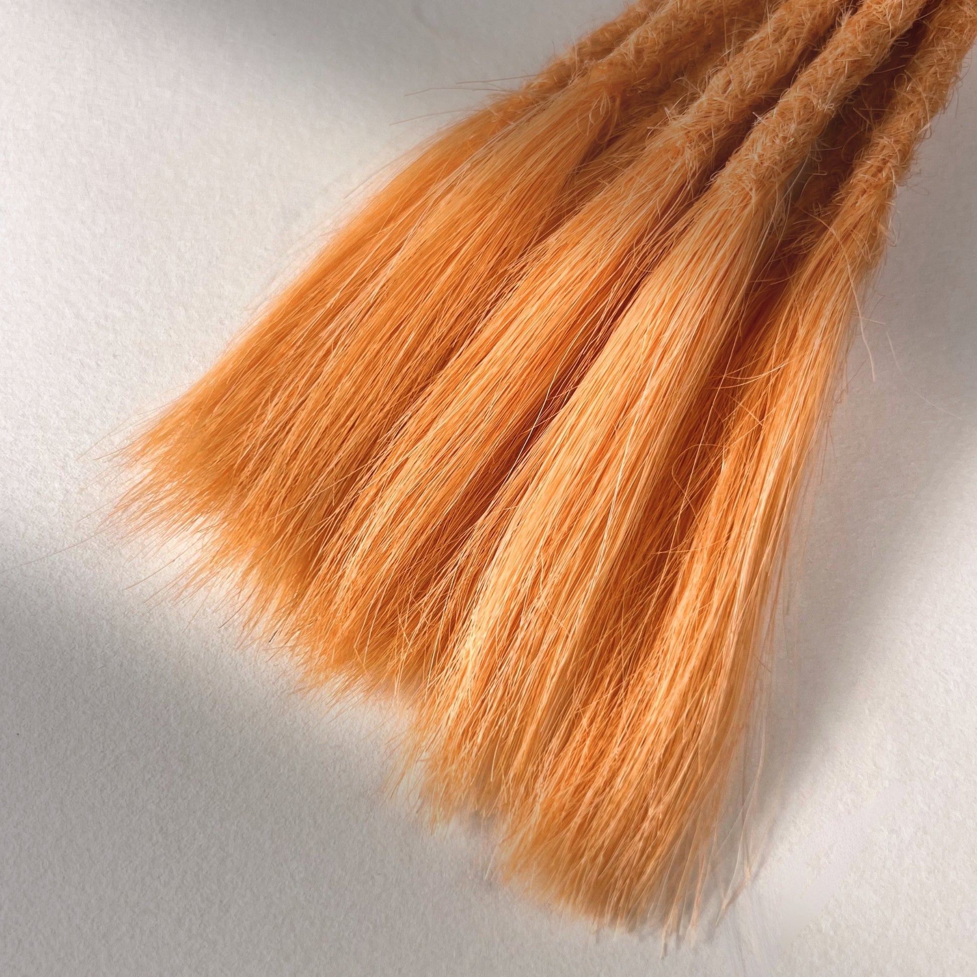 Tip detail of straight loc extensions with open ends in Peach Orange.