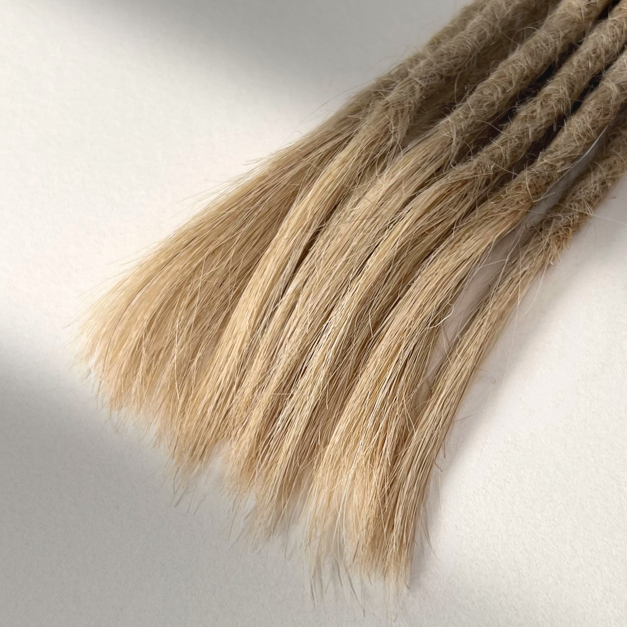 Tip detail of straight loc extensions with open ends in Sunlit Blonde.