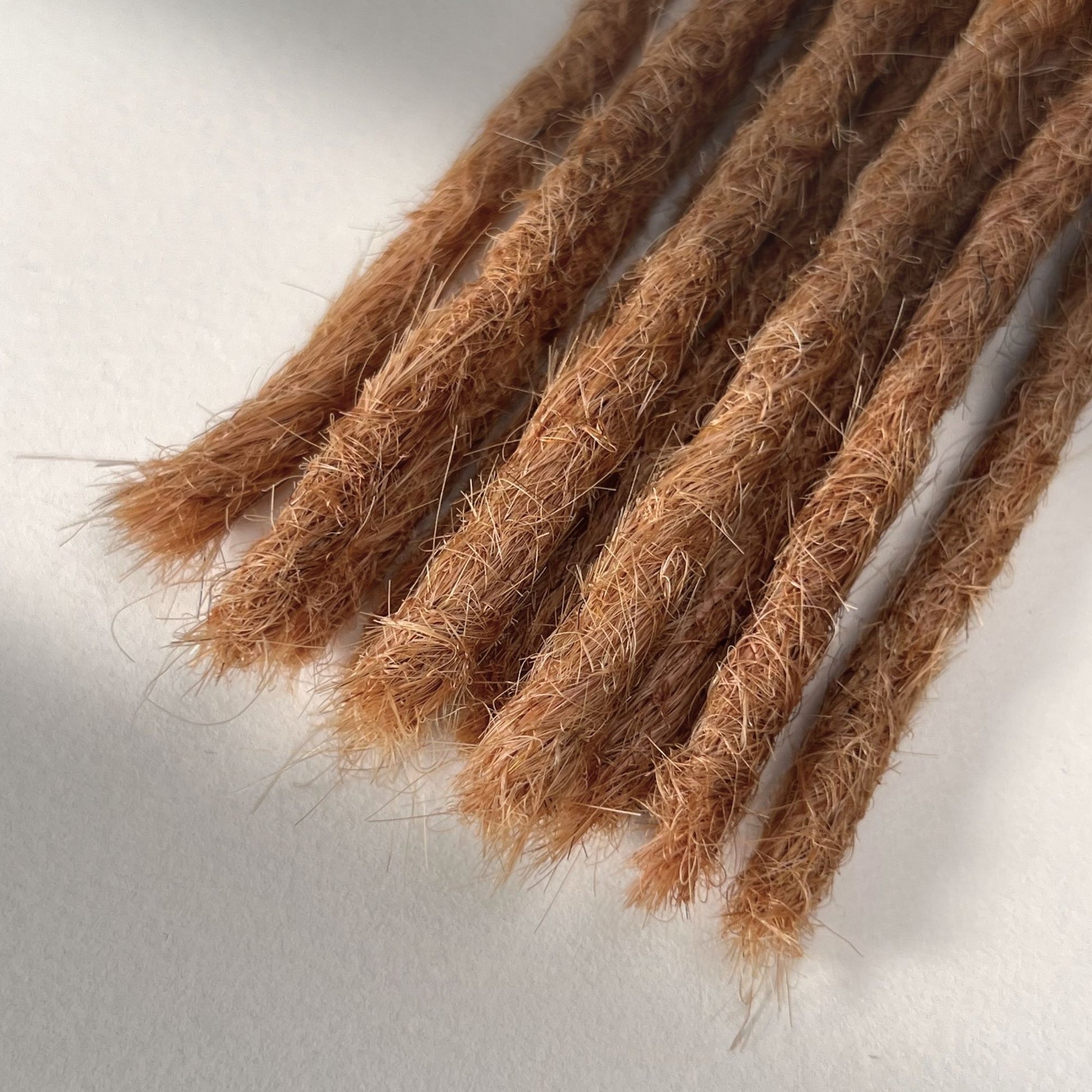 Tip detail of straight loc extensions with blunt ends in Warm Copper Blonde.