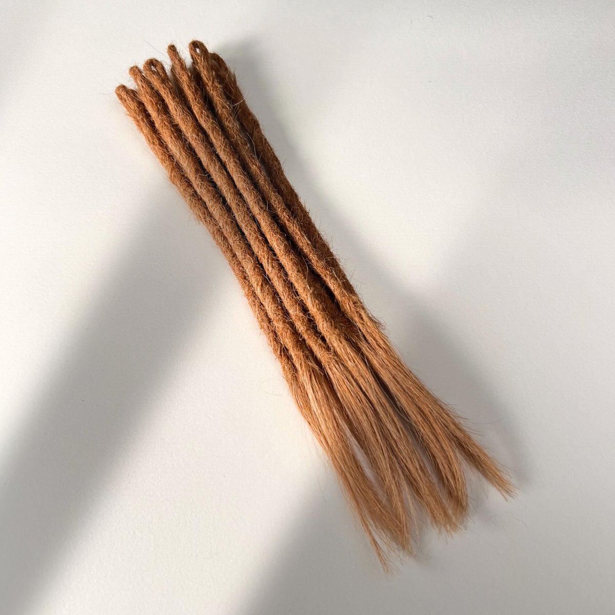 Full view of temporary single-ended straight loc extensions with open ends in Warm Copper Blonde.