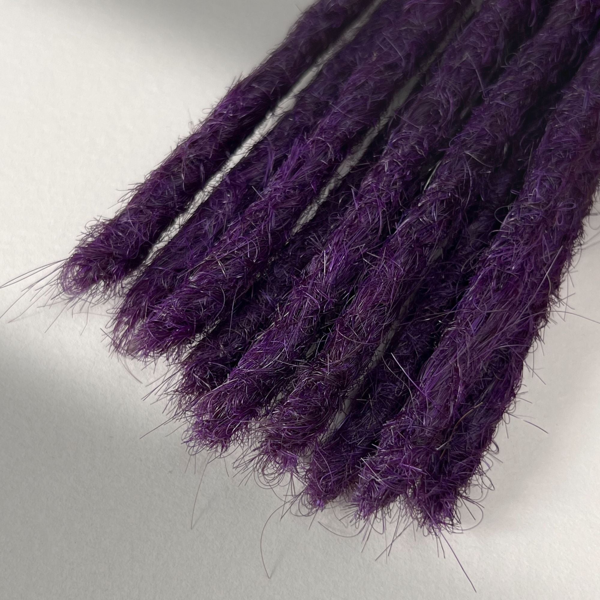 Tip detail of straight loc extensions with blunt ends in Electric Violet.