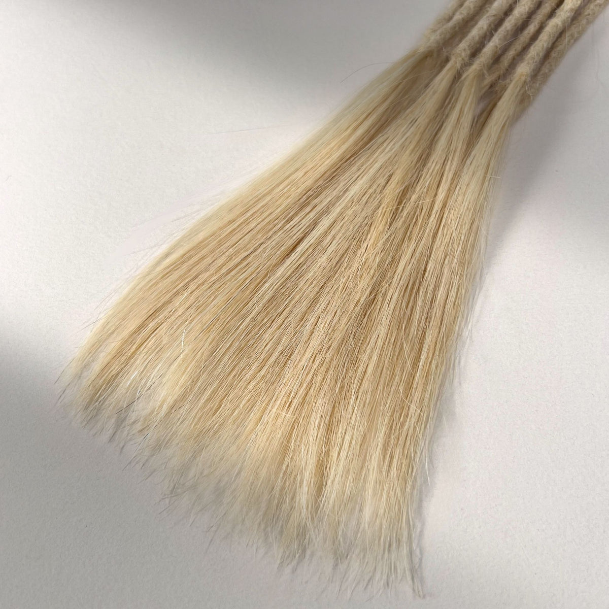 Tip detail of straight loc extensions with long loose ends in Wheat Blonde.